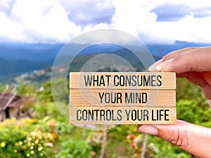 Motivational inspirational quote. What consumes your mind, controls your life on wooden blocks with nature background.