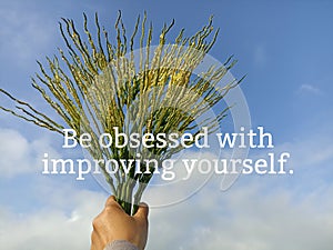 Motivational quote - Be obsessed with improving yourself. With palm tree flowers in hand on blue sky background.