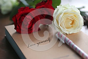 Motivational quote - Love yourself. Self love and care concept written on a book cover, with a pen, red and white roses background