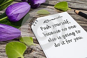 Motivational quote on notepad with flowers on wooden desk.