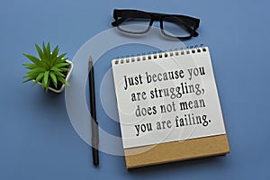 Motivational quote on notepad with potted plant, glasses and a pen