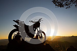 motocross bike against beautiful lights, silhouette of a motocross motorcycle On top of rock high mountain at beautiful sunset,