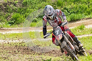 Motocross. Motorcyclist rushes along a dirt road, dirt flies from under the wheels. Against the backdrop of bright spring greens.