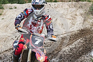 Motocross. Motorcyclist rushes along a dirt road, dirt flies from under the wheels. Against the backdrop of bright spring greens.