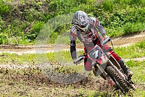 Motocross. Motorcyclist rushes along a dirt road, dirt flies from under the wheels. Against the backdrop of bright spring greens.