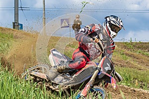 Motocross. Motorcyclist rushes along a dirt road, dirt flies from under the wheels. Green vegetation and blue sky.