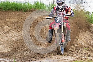 Motocross. Motorcyclist rushes along a dirt road. Greenery in the foreground.