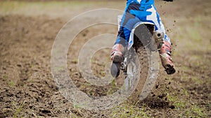 Motocross racer start riding his dirt Cross MX bike kicking up dust rear view, close up