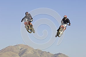 Motocross Racers Performing Stunt In Midair Against Blue Sky