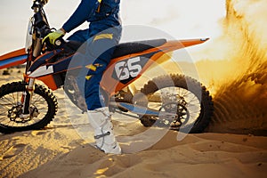 Motocross rider skidding wheel raising sand dust