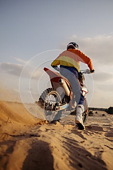 Motocross rider skidding wheel raising sand dust