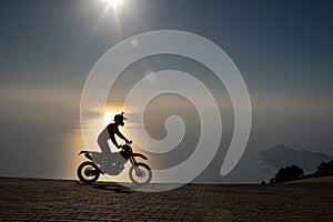 Motocrosser riding motorcycle by the sea at sunset