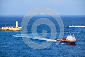 A motor boat enters to the Grand Harbour near the Saint Elmo Lighthouse, Valletta.