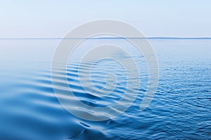 Motor boat leaves small waves behind boat in the blue sea. Evening view of sea bay at sunset.