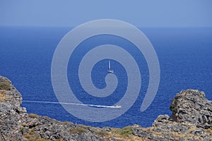 A motor boat and a sailboat are sailing on the Mediterranean Sea near the coast of Lindos.