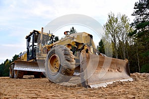 Motor Grader on road construction in forest area. Greyder leveling the sand, ground and gravel during road work. Heavy machinery