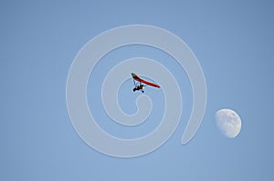 Motor hang glider flying free in the daytime sky with the moon