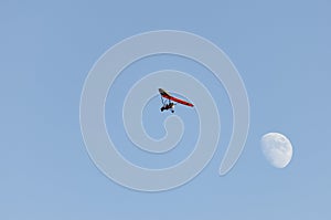 Motor hang glider flying free in the daytime sky with the moon