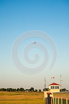 Motor hang glider with passengers flying over aerodrome in clear blue sky