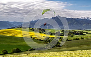 Motorový paragliding cez zelené poľnohospodárske polia a hory v krásnej krajine