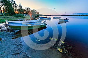 Motor and row boats anchored on the calm summer lake, sunset time, boats reflected in the water. sunset and electrical light