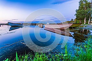 Motor and row boats anchored on the calm summer lake, sunset time, boats reflected in the water. Northern Sweden