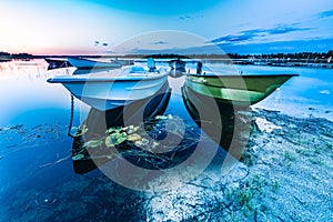 Motor and row boats anchored on the calm summer lake, sunset time, boats reflected in the water. Stocksjo Lake, close to Umea city