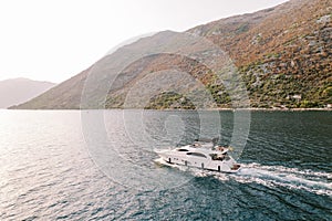 Motor single-deck yacht sails along the sea along the mountain coast