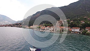 Motor yacht sails along the Bay of Kotor past the Prcanj coast