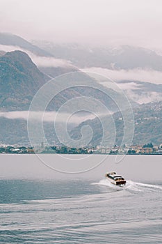 Motor yacht sails on Lake Como towards the mountainous coast in fog. Italy