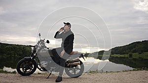 Motorbike driver talking on his phone sitting on a scrambler by lake in autumn