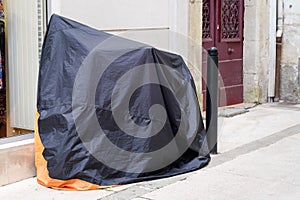 Motorbike protected by protective cover in street motorcycle with dark grey orange tarpaulin jacket