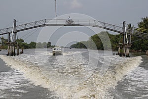 Motorboats pass under the bridge on the Mesuji River. There\'s a motorbike crossing over the bridge