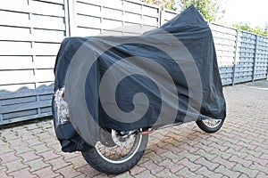 Motorcycle covered with grey cover near the wall in the street