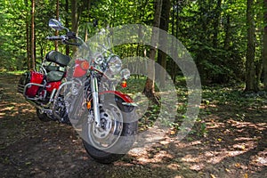 Motorcycle cruiser stands on dirt road in sunny green forest. Walk ride on chopper in forest road