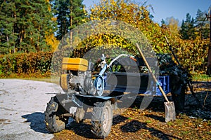 Motorcycle cultivator standing against the trees with green and yellow foliage. Autumn works on the improvement of the territory