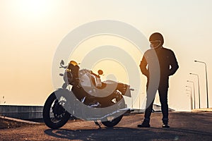 Motorcycle driver in a helmet and leather jacket stands on the road next to a sports motorcycle