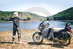 Motorcycle driver stands with his arms outstretched. for a meeting of adventures on the dirt beach mountain river, enduro, off