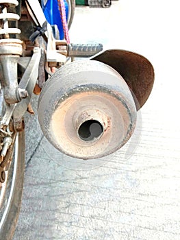 Motorcycle end exhaust pipe at frame on blurred cement flooring closeup.