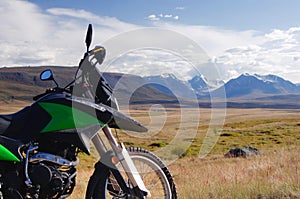 Motorcycle enduro traveler alone under a blue sky with white clouds on a background of mountain valley with snow ice covered peak