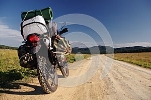 Motorcycle enduro traveler with suitcases standing on stone dirt road path on a mountain plateau with the green grass