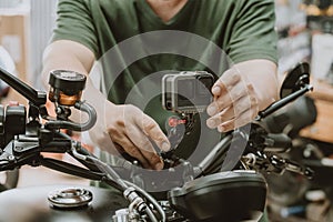 Motorcycle mechanic installing action sports camera into motorcycle handle bar at garage .maintenance,repair concept in garage .