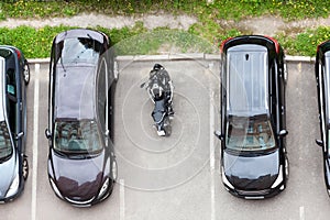 Motorcycle is parked on vehicle parking space between several cars. Top view