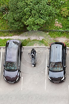 Motorcycle is parked on vehicle parking space between two passenger cars. Top view, vertical