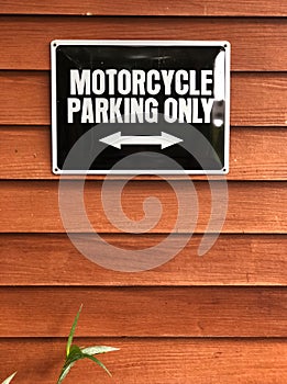 Motorcycle parking sign on wooden wall. Black sign and white color text `Motorcycle parking only`