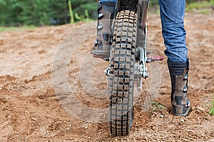 Motorcycle racer with boots standing on peg of dirt bike on sandy track