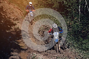 motorcycle racer on an enduro sports motorcycle rides on a muddy road with puddles in the forest in an off-road race