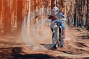 motorcycle racer on an enduro sports motorcycle rides fast on a dusty road in the forest in an off-road race photo