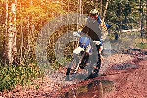 motorcycle racer on an enduro sports motorcycle rides on a muddy road in the forest in an off-road race photo