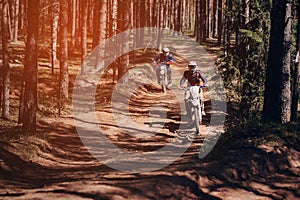 Motorcycle racers on enduro sports motorcycles are driving fast on a dusty road in the forest in an off-road race photo